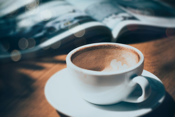 cup of coffee with magazine on table in cafe in dark tone and vintage .