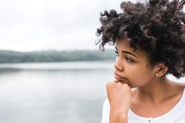 Close-up shot of young black woman with pensive look, against nature background with copy space for your text or advertising content. POrtrait of dark-skinned female wearing casual posing outdoor