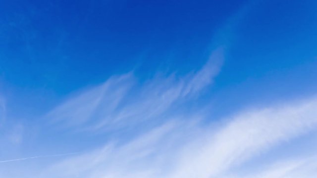 Rapidly moving white cirrus cloud and vapour trails formed by jet aircraft in a blue sky timelapse