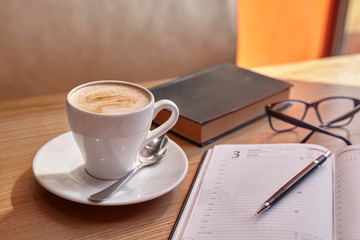 Mug with a saucer with cappuccino coffee on a diary with a handle with glasses on a wooden table in a coffee house