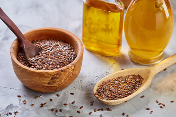 Flax seeds in bowl and flaxseed oil in glass bottle on wooden background, top view, close-up, selective focus