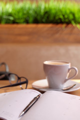 Mug with a saucer with cappuccino coffee on a diary with a handle with glasses on a wooden table in a coffee house