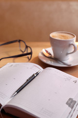 Mug with a saucer with cappuccino coffee on a diary with a handle with glasses on a wooden table in a coffee house
