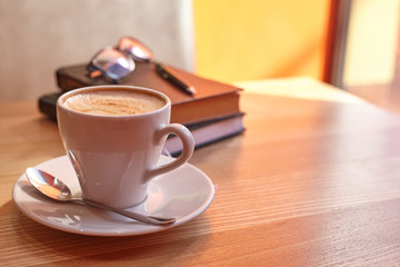 Mug with a saucer with cappuccino coffee on a diary with a handle with glasses on a wooden table in a coffee house