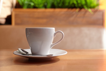 White coffee mug on a saucer with a spoon on a wooden table in a coffee house