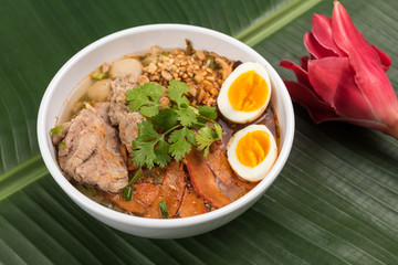 Spicy noodle soup with pork and egg in bowl on banana leaf