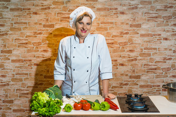 Happy woman in chef uniform on the kitchen with vegetables.