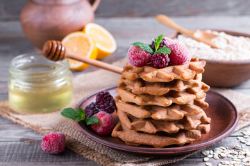 Homemade oatmeal waffles with berries and honey on a old wooden table