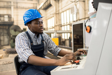 Portrait shot of highly professional worker wearing checked shirt and overall operating machine at...