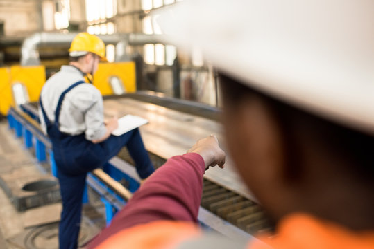 Multi-ethnic team of technicians wearing hardhats and uniform carrying out inspection at production department of modern plant, one of them taking necessary notes