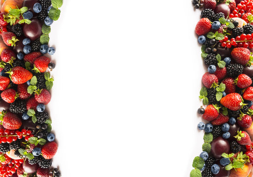 Mix berries and fruits at border of image with copy space for text. Black-blue and red food. Ripe blackberries, blueberries, strawberries, red currants and plums on white background. Top view.