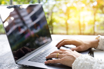 Closeup business woman's hands typing on laptop keyboard on desk with sunlight.