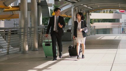 Two business people walking and drag the baggage along open passage