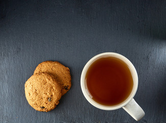 A glass cup of black tea with cookies on a dark greyish marble background. Breakfast background