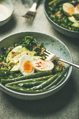 Healthy vegetarian breakfast bowls. Quinoa, kale, green beans, avocado, egg and tahini dressing bowls over concrete background, selective focus. Energy boosting, diet food concept
