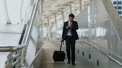 The Asian businessman walking dragging luggage to exit with hastiness - obrazy, fototapety, plakaty