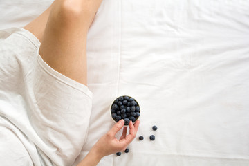 Healthy eating concept. Woman having blueberries in bed. Top view.