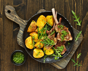 Chops of lamb on bone, with baked potatoes and pesto sauce.