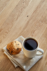 Porcelain teacup with chocolate chips cookies on cotton napkin on a rustic wooden background, top view