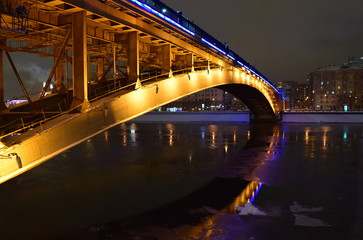 Brightly illuminated bridge at night in winter. Reflections in the river. Moscow. Urban landscape.