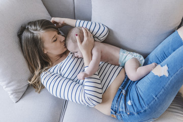 Young mother holding her newborn child. Woman and new born boy relax. Family at home. Portrait of happy mother and baby. Young beautiful mom lying at bed with a cute little child.