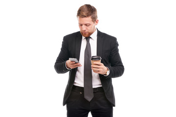 Portrait of young businessman holding paper coffee cup and using cell phone