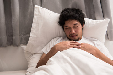 Laziness of Asian man that still sleeping on the bed in bedroom in morning, time to wake up.