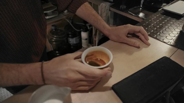 Cinemagraph, eternal video loop of professional barista in downtown cafe or coffee shop agitates cup of freshly brewed espresso,to mix flavors and get rid of air bubbles, to add steamed milk for latte