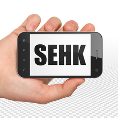 Stock market indexes concept: Hand Holding Smartphone with  black text SEHK on display,  Tag Cloud background, 3D rendering