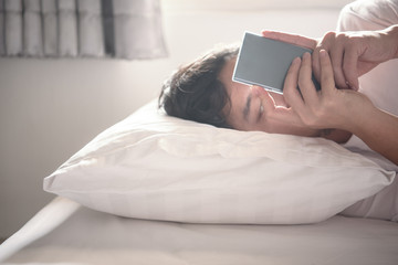 Asian man using phone typing message to chatting in social network while lying on the bed in bedroom