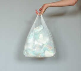 Woman hand holding a plastic bag full of dirty used baby diapers