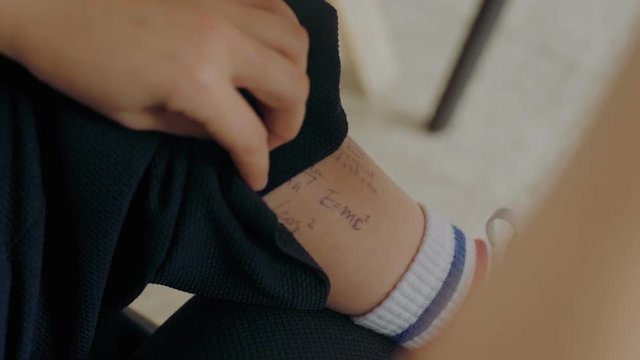 Smart and cheating student pulls up pants to check on cheat sheet formulas written down on leg skin during exam or test period in high school or university.