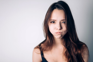 Fototapeta premium Indoor shot of cute girl, having doubtful and indecisive face expression, pursuing her lips as if forbidden to say anything.