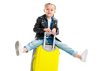 Little tourist with extended legs sitting on yellow wheel suitcase isolated on white