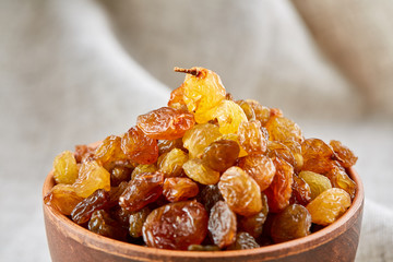 Wooden bowl with golden raisins on light tablecloth, close-up, selective focus