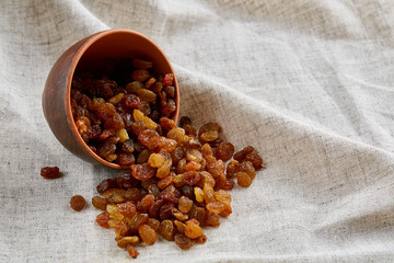Wooden bowl with golden raisins on light tablecloth, close-up, selective focus