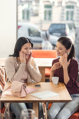 Engagement ring. Happy positive young woman shoeing her hand and pointing at ring while telling her friend about engagement