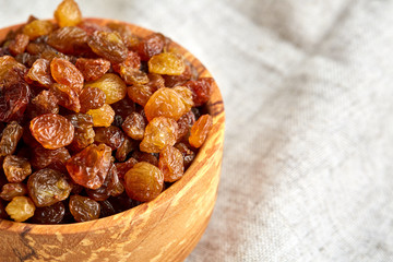 Wooden bowl with golden raisins on light tablecloth, close-up, selective focus
