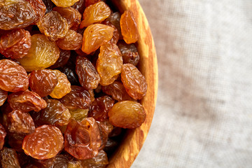 Wooden bowl with golden raisins on light tablecloth, close-up, selective focus