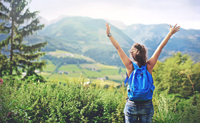 woman tourist enjoys the beautiful scenery of the Alpine mountains, stands with her back and raises her hands