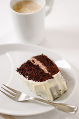 Cup of coffee with one piece chocolate cake and dessert fork on white background