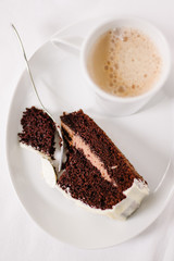 Cup of coffee with one piece chocolate cake and dessert fork on white background