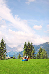 young woman tourist with a backpack and glasses resting on green grass and admiring the alpine mountains and meadows