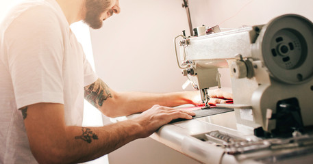 Young stylish man with tattoo tailor working on new clothing