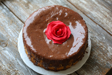 Handmade sponge cake with chocolate frosting. Small cake with cacao ganache glaze. Red sugar rose decorated. Homt pastry. Sweet dessert. Cute birthday cake present.