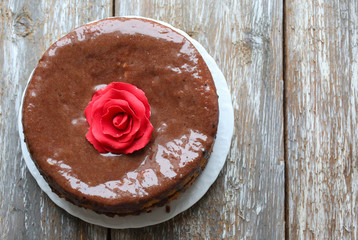 Handmade sponge cake with chocolate frosting. Small cake with cacao ganache glaze. Red sugar rose decorated. Homt pastry. Sweet dessert. Cute birthday cake present.