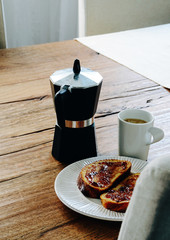 French toasts covered with jam laying on white plate. Coffee mug and coffee maker moka pot standing...