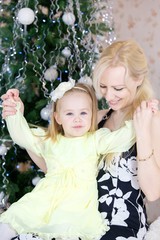 Cheerful mom and cute baby girl against the background of Christmas decorations.