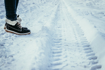 Reifenspuren im Schnee, Winterschuhe einer jungen Frau