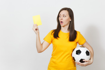 European serious severe young woman, football referee or player in yellow uniform showing yellow card, holding soccer ball isolated on white background. Sport play football, healthy lifestyle concept.